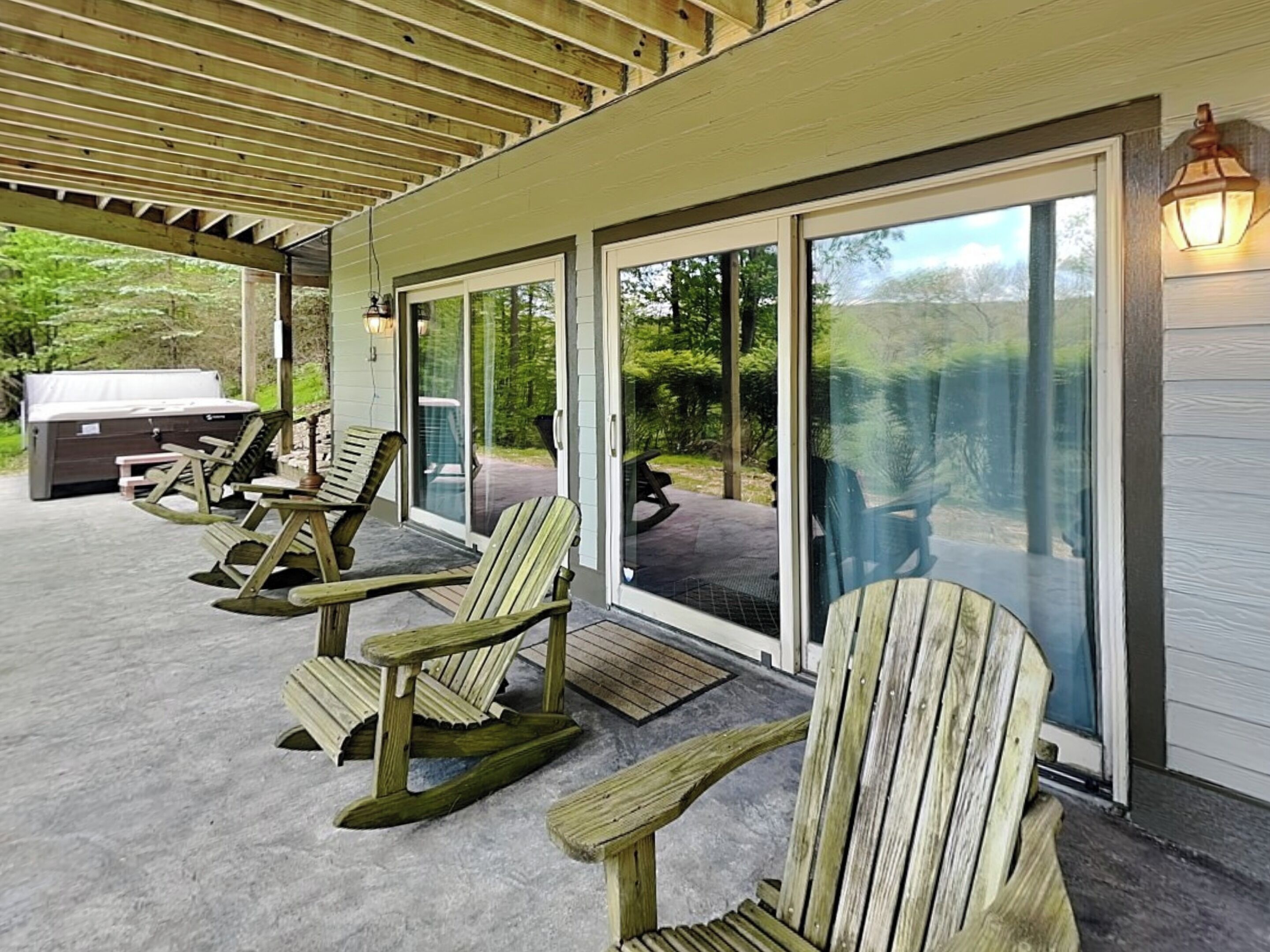 Une terrasse couverte avec des fauteuils à bascule en bois, un barbecue et une vue sur l’extérieur.