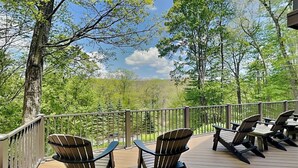 A deck with Adirondack chairs and a table, overlooking a forested area. - Canadian Day by Taylor Made Deep Creek (McHenry)