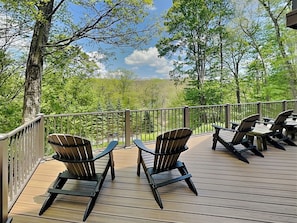 Eine Terrasse mit Adirondack-Stühlen und einem Tisch, mit Blick auf ein bewaldetes Gebiet.