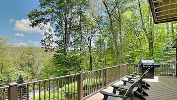 A deck with picnic tables and a grill, overlooking a forested area.