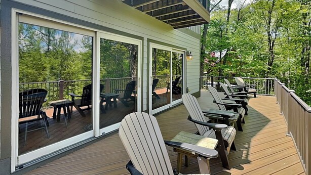 A deck with Adirondack chairs, a table, and a glass door leading to a deck area. - Canadian Day by Taylor Made Deep Creek (McHenry)