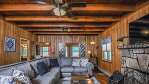A cozy living room with a sectional sofa, a coffee table, a fireplace, and wooden walls. - Canoe Cottage by Taylor Made Deep Creek (Oakland)