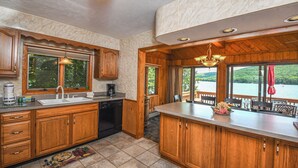 A kitchen with wooden cabinets, a dishwasher, and a large window overlooking a lake. - Canoe Cottage by Taylor Made Deep Creek (Oakland)