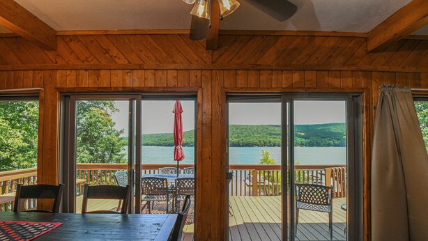 A wooden interior with a stone floor, large sliding glass doors to a deck, and a table with chairs. - Canoe Cottage by Taylor Made Deep Creek (Oakland)
