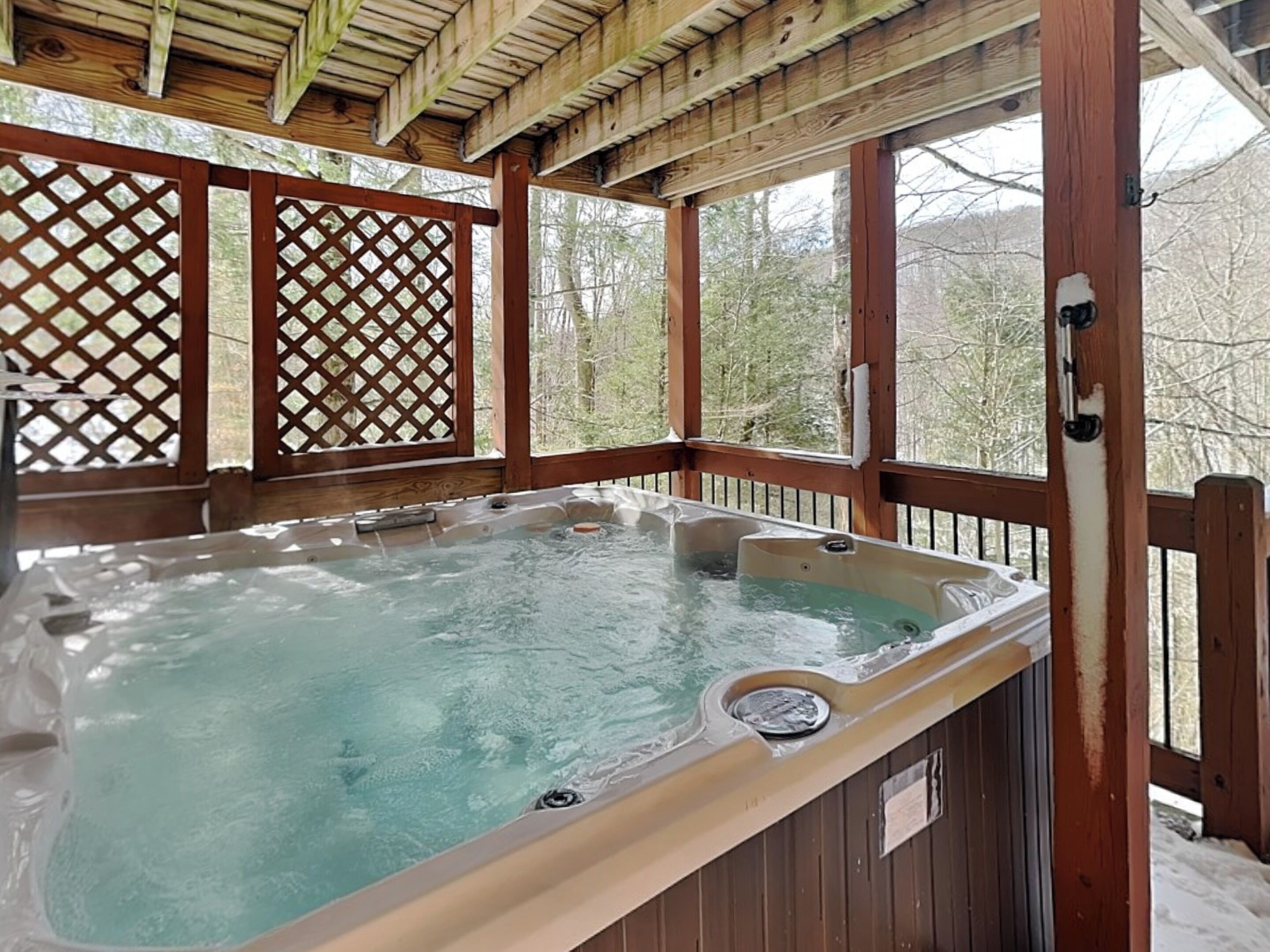 A hot tub in a wooden deck with lattice panels and a view of trees.