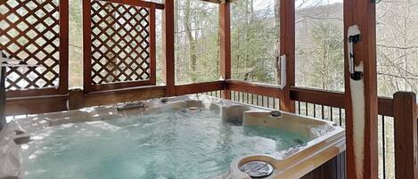 Ein Whirlpool auf einer Holzterrasse mit Gitterverkleidung und Blick auf Bäume.