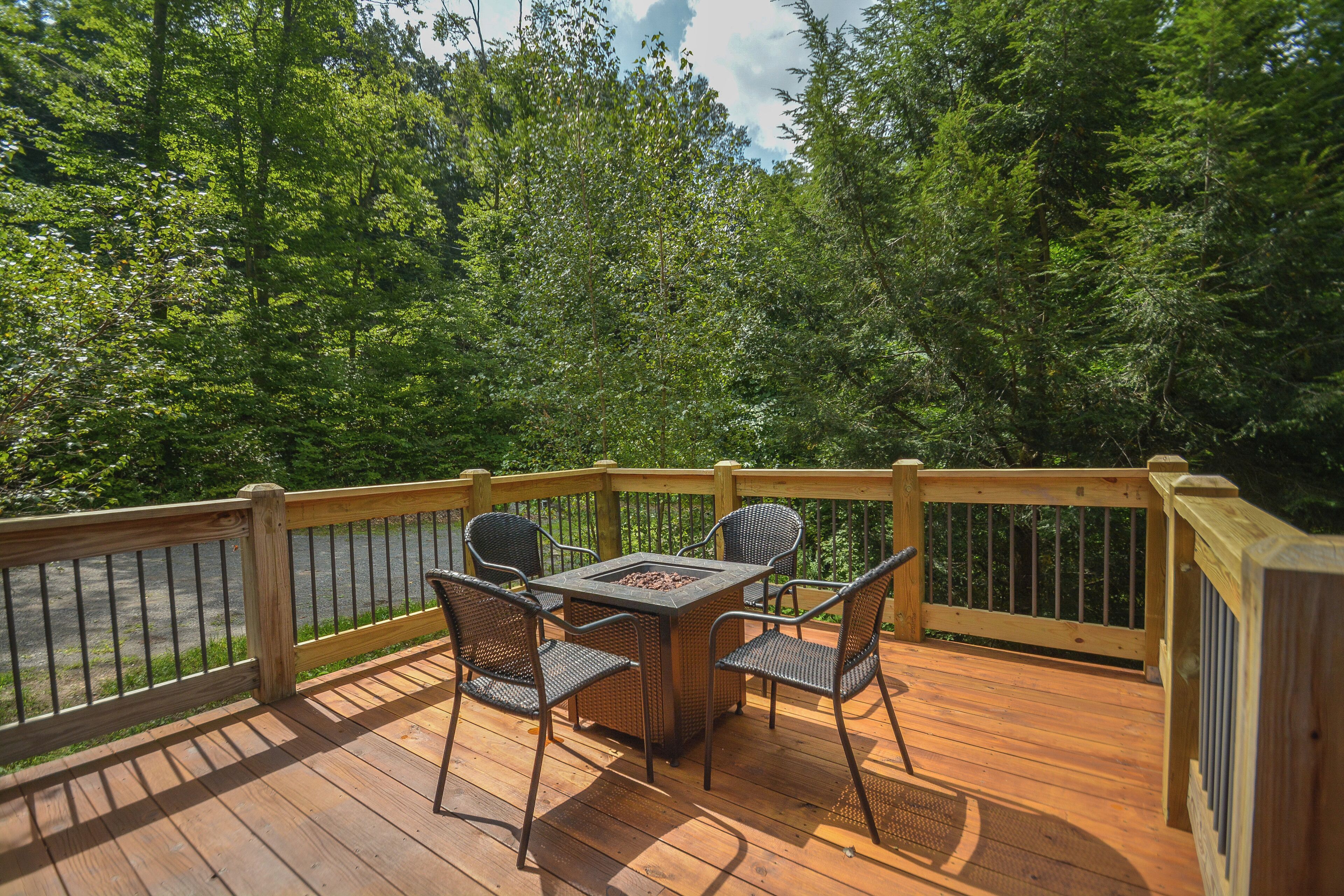 A wooden deck with a table and chairs, surrounded by a wooden railing, overlooking a forested area.