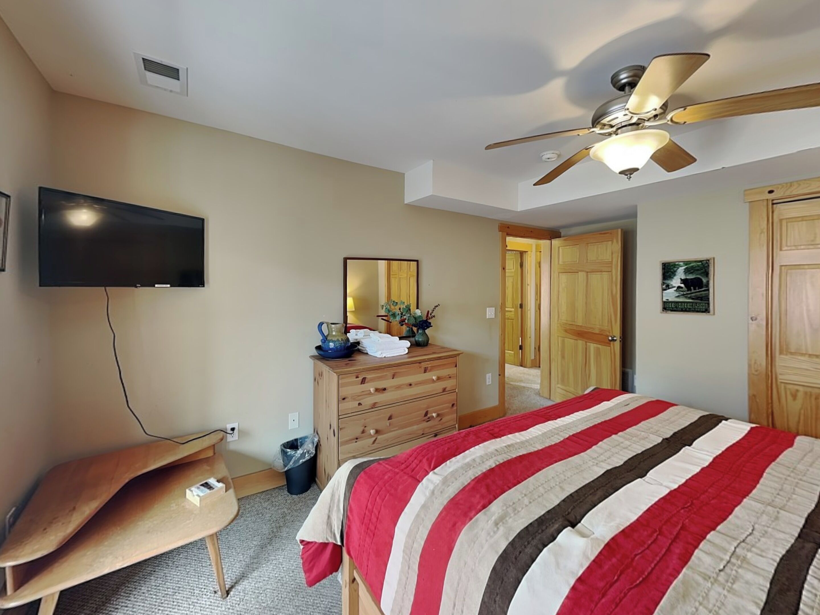 A bedroom with a bed, a ceiling fan, a TV, a dresser, and a door.