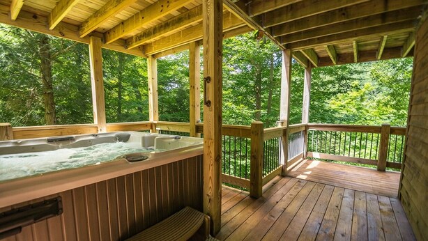 Une terrasse en bois dotée d’un jacuzzi et d’un espace salon, le tout entouré d’arbres.