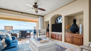 Ein geräumiges Wohnzimmer mit Balkon, Deckenventilator, Flachbildfernseher und einer großen Topfpflanze.