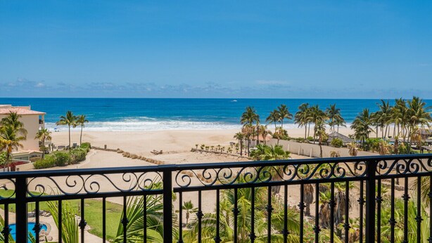 Blick auf einen Strand von einem Balkon aus, mit Palmen und blauem Himmel.