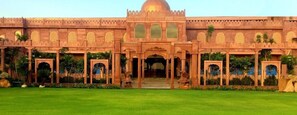 A large, ornate building with a central dome and multiple arches, surrounded by a well-maintained lawn. - Amritam Palace (Jodhpur)