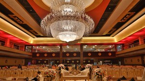A grand hall with tiered seating, a large chandelier, and ornate floral arrangements. - Amritam Palace (Jodhpur)