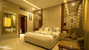 A hotel room with a large bed, a sitting area with a chair, a wooden coffee table, and a decorative partition with geometric patterns. - Amritam Palace (Jodhpur)