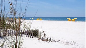 Ein sandiger Strand mit gelben Sonnenschirmen und einem Holzzaun.
