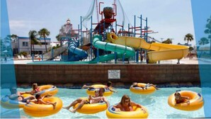 Ein Wasserpark mit Wasserrutsche, Schwimmbecken mit Personen auf Luftmatratzen und einem Rettungsschwimmturm.