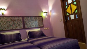 A bedroom with two beds, patterned wall decor, and a wooden door with stained glass. - Gite Talassemtane, a cosy guesthouse in the middle of nature in Chefchaouen area (Chefchaouen)