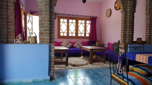 A room with a purple sofa, a wooden table, a patterned rug, and a brick wall. - Gite Talassemtane, a cosy guesthouse in the middle of nature in Chefchaouen area (Chefchaouen)
