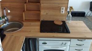 Moderni keittiö, jossa on valkoiset kaapit, puinen työtaso, sisäänrakennettu liesi ja pesuallas.