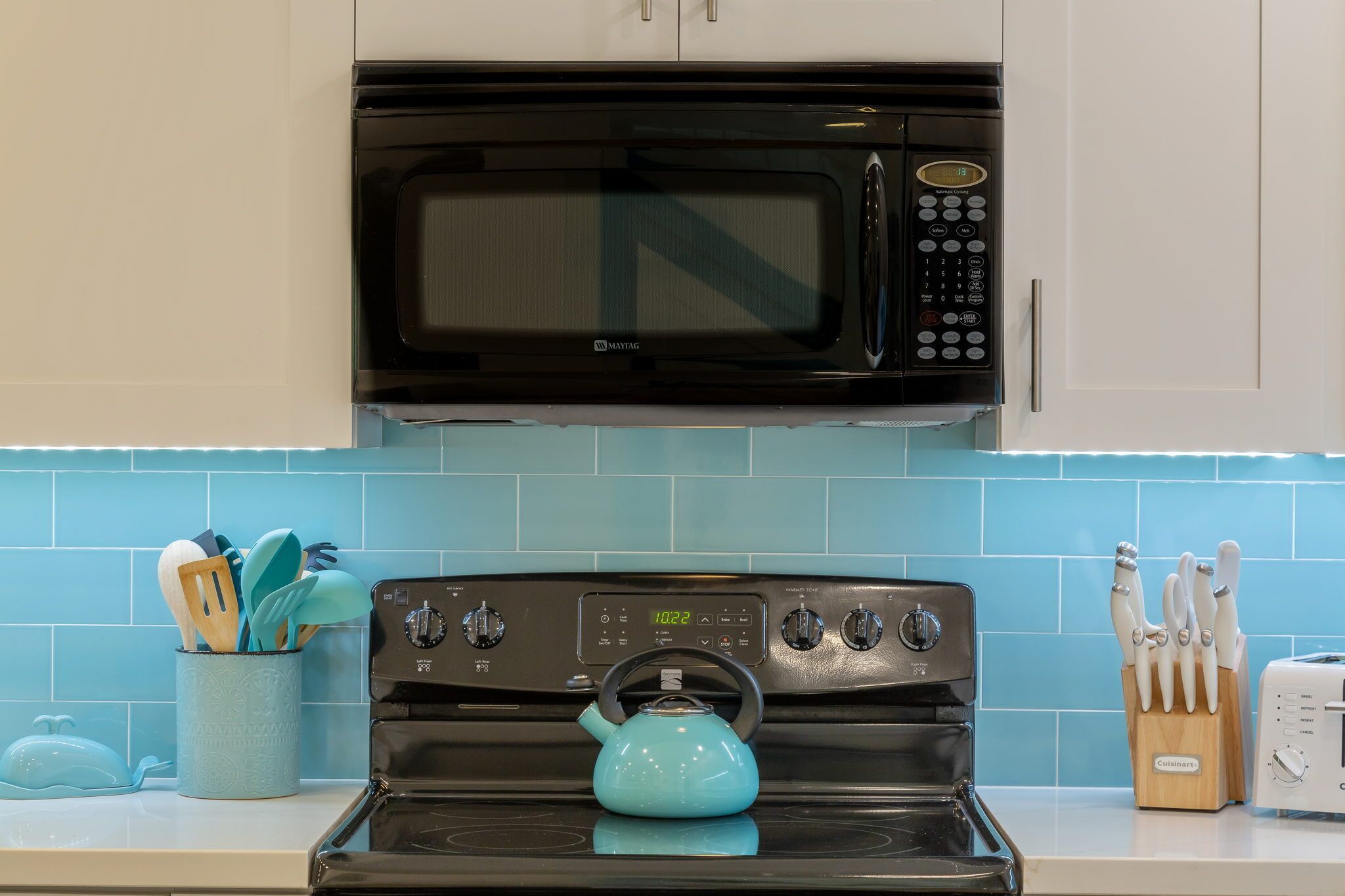 A kitchen with a black microwave, a teal kettle, and a toaster on the counter.