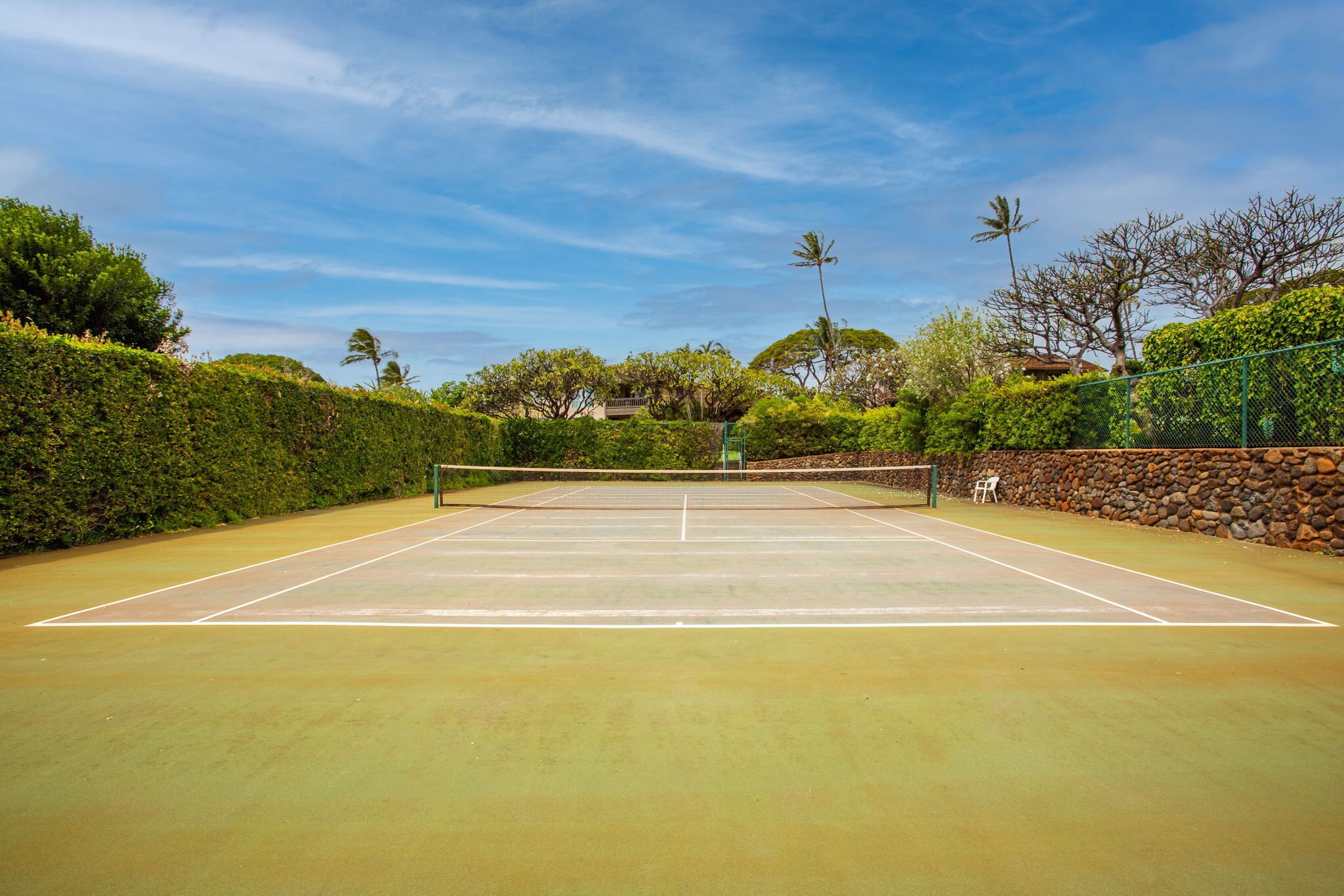 An outdoor tennis court with a stone wall and greenery on one side.
