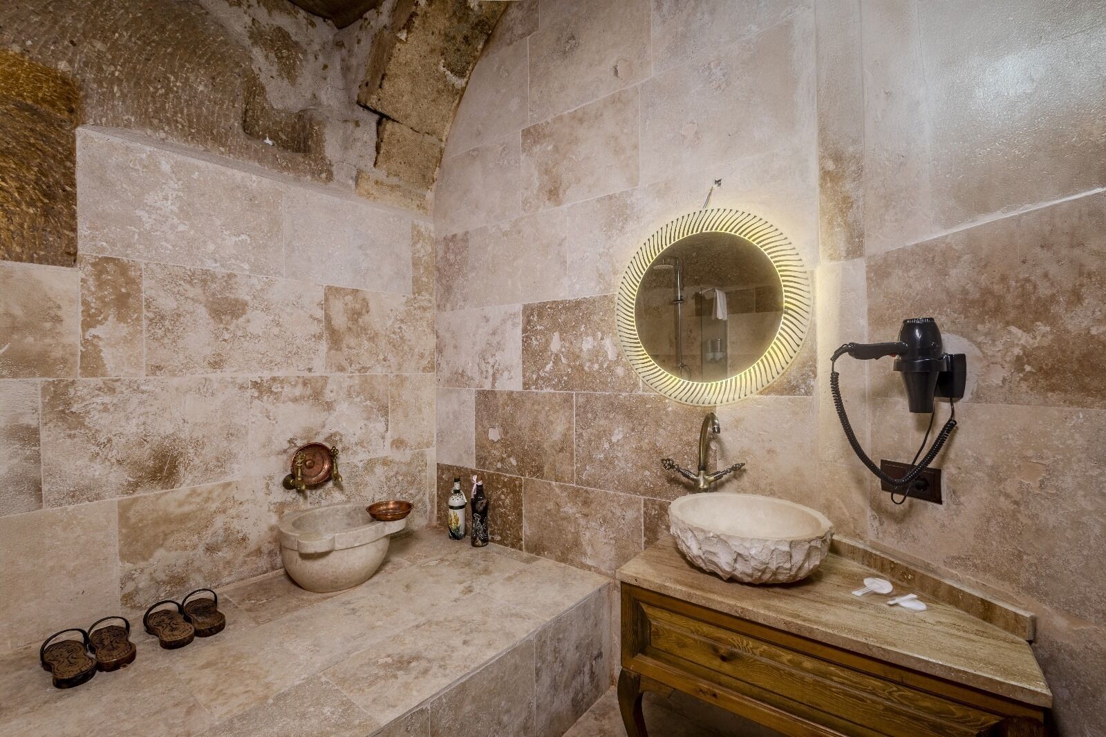A bathroom with a stone sink, a round mirror, and a hairdryer mounted on the wall.