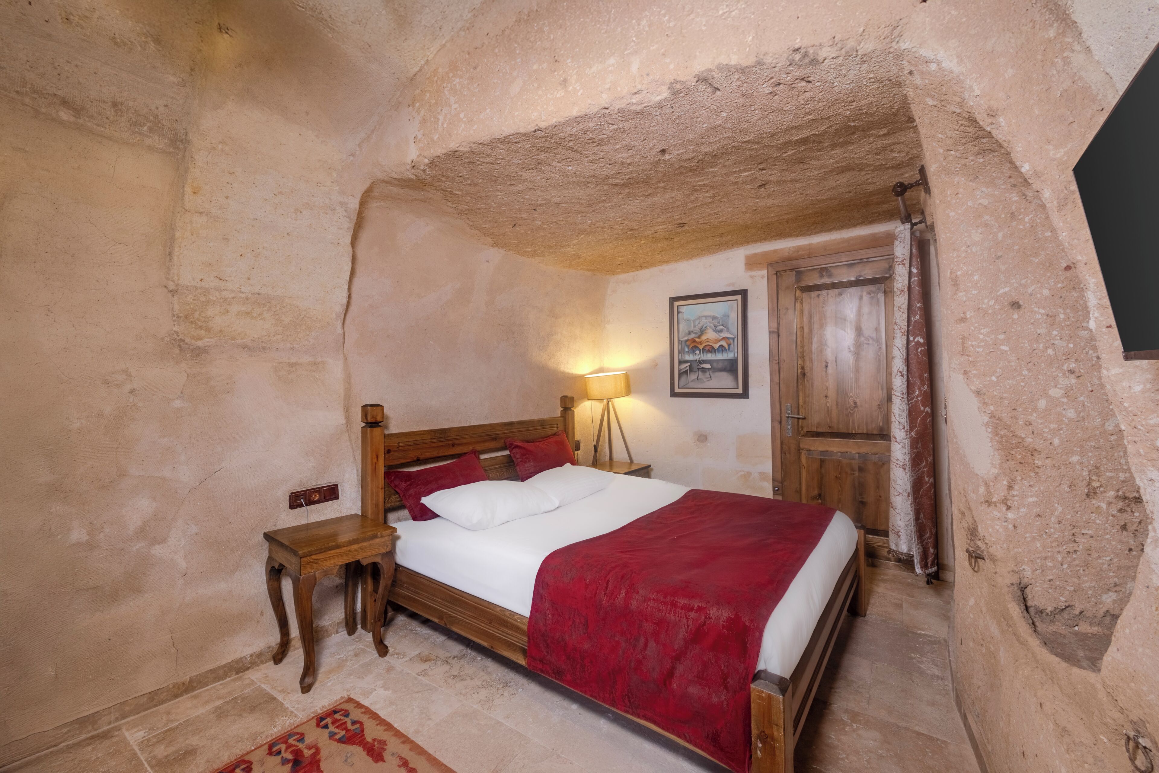 A bedroom with a wooden bed, a nightstand, a lamp, and a door.