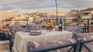 A table set with wine glasses, plates, and a bowl of fruit, overlooking a cityscape. - Zula Cave House (Ürgüp)