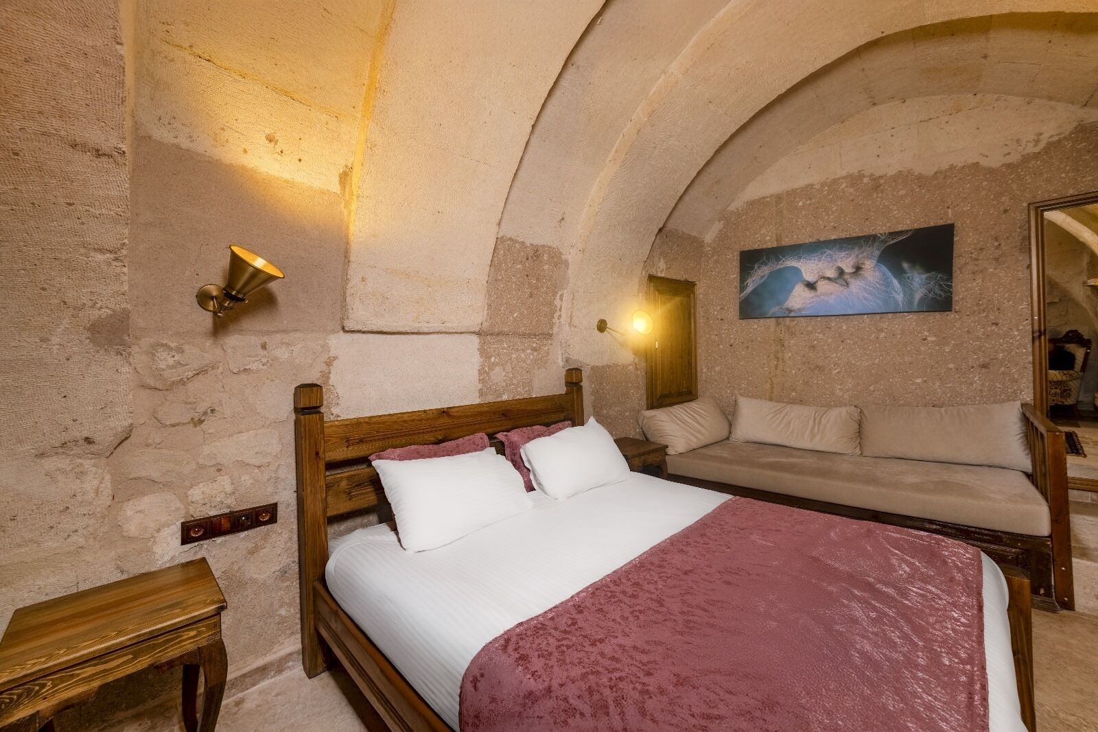 A bedroom with a wooden bed, a sofa, and a painting on the wall.