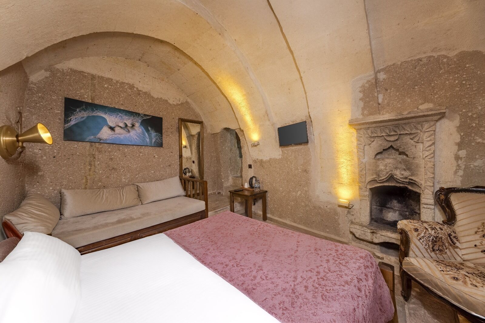 A cozy room with a bed, a sofa, a fireplace, and a painting on the wall.