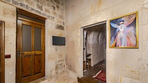 A stone-walled hallway with a wooden door, a small stool, and a painting on the wall. - Zula Cave House (Ürgüp)