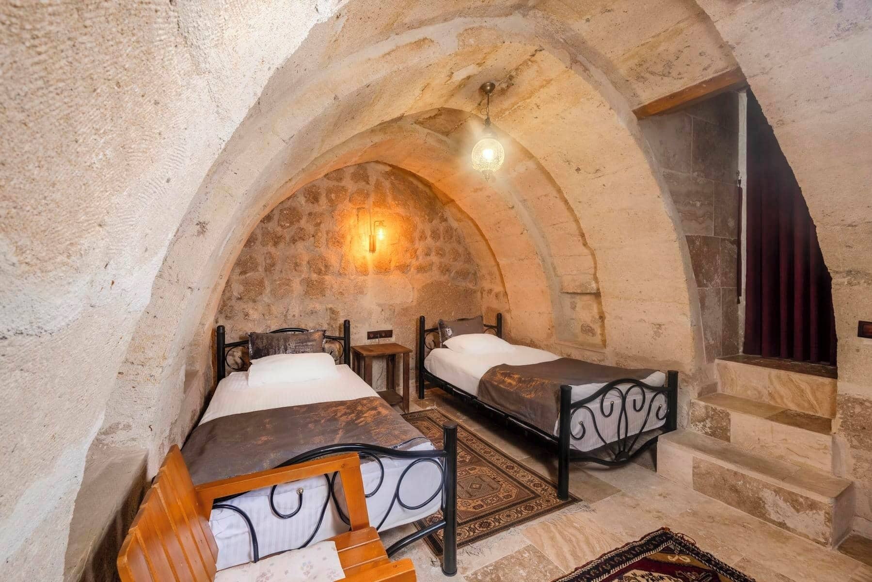 A room with two beds, stone walls, and a stone staircase.