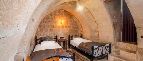 A room with two beds, stone walls, and a stone staircase.