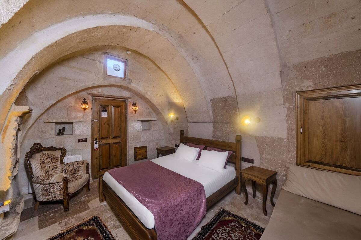 A rustic bedroom with a stone ceiling, a wooden bed, a chair, and a nightstand.