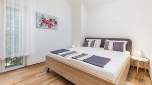A bedroom with a bed, a bedside table, a window with curtains, and a floral painting on the wall. - Apartman u Volme, Medulin (Banjole)