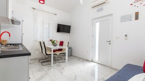 A modern hotel room with a kitchen area, a dining table with chairs, a TV mounted on the wall, and a door with a calendar and notes on the wall. - Apartman u Volme, Medulin (Banjole)