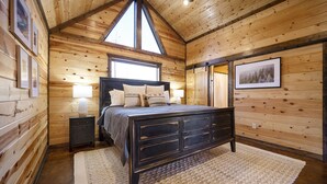Camera da letto in una baita di legno, con un letto, comodini e un'ampia finestra.