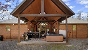 Una baita di legno con un portico coperto, posti a sedere all'aperto, una vasca idromassaggio e un caminetto.