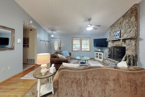 A living room with a stone fireplace, a ceiling fan, a TV, and a couch. - Carefree Cove by Taylor Made Deep Creek (Swanton)