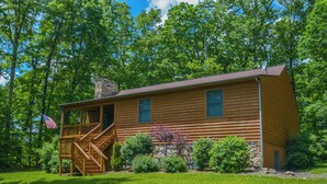 A wooden cabin with a stone chimney, a wooden deck, and a flag. - Carefree Cove by Taylor Made Deep Creek (Swanton)