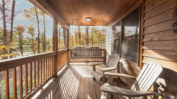 A wooden porch with Adirondack chairs, a bench, and a view of autumn trees. - Carefree Cove by Taylor Made Deep Creek (Swanton)