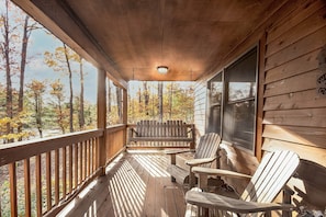 A wooden porch with Adirondack chairs, a bench, and a view of autumn trees. - Carefree Cove by Taylor Made Deep Creek (Swanton)