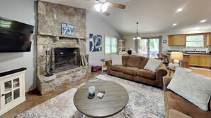 A living room with a stone fireplace, a television, a brown sofa, and a round coffee table. - Carefree Cove by Taylor Made Deep Creek (Swanton)