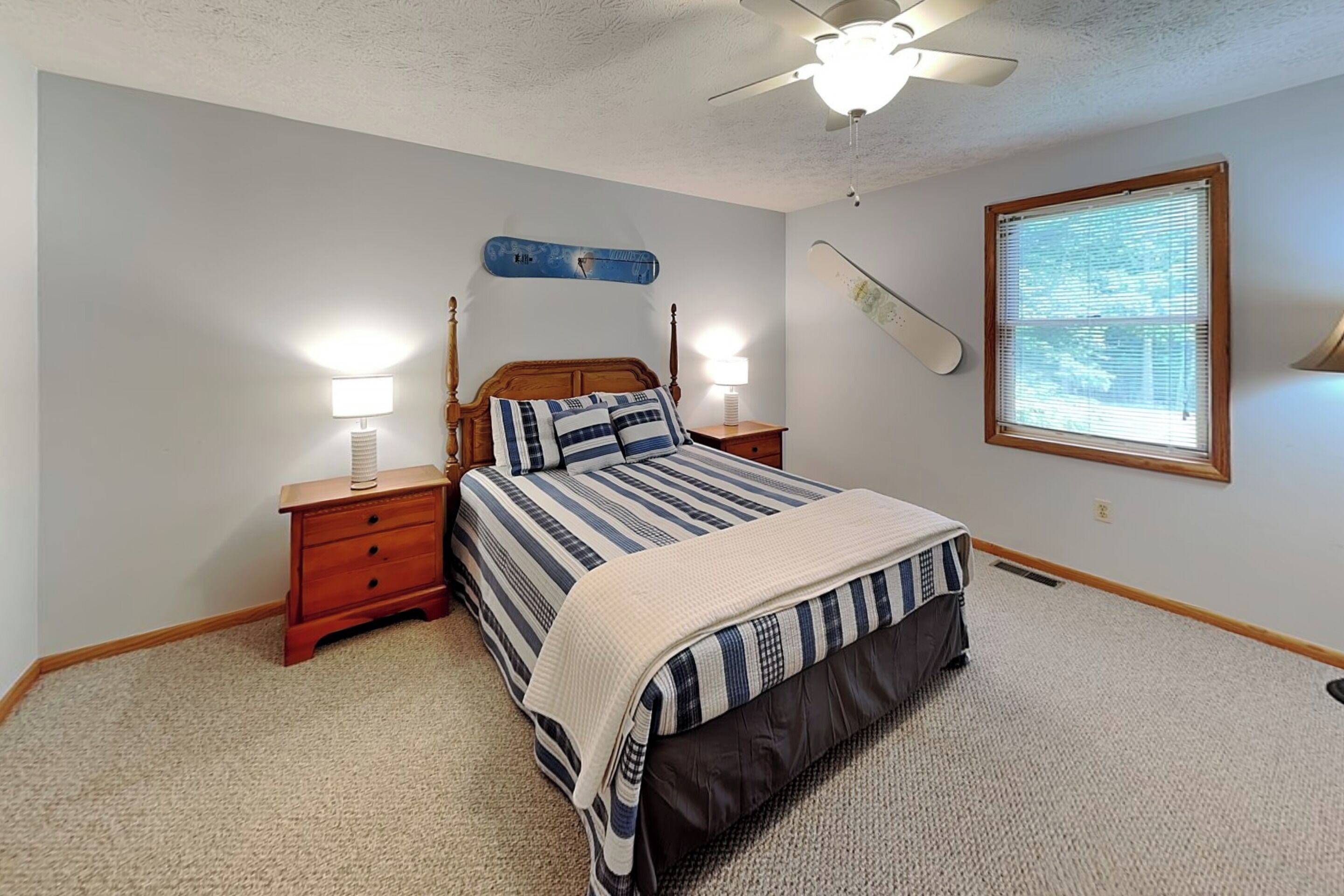 A bedroom with a bed, nightstands, a ceiling fan, a window with blinds, and a wall-mounted shelf.