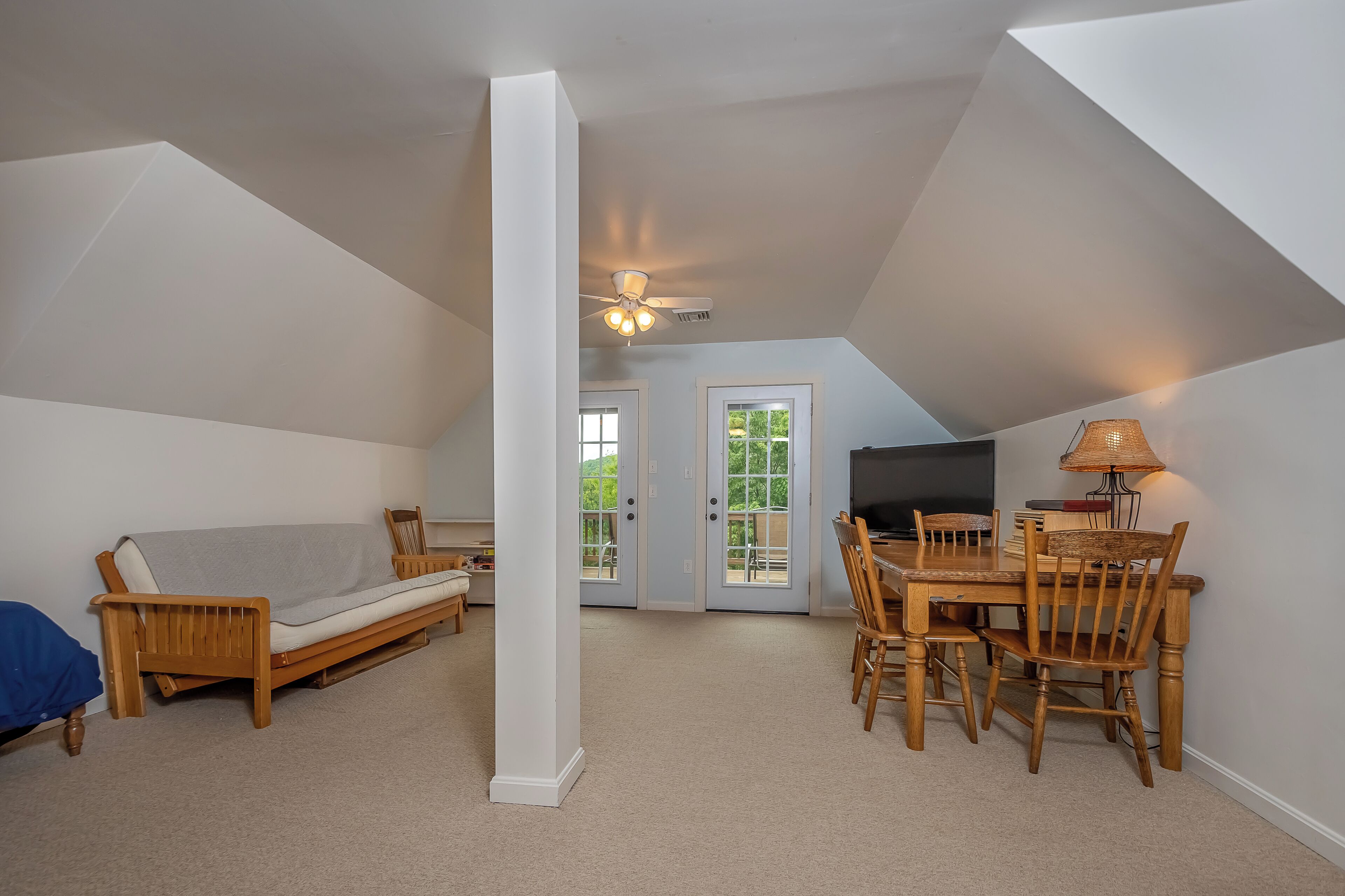 A loft-style room with a ceiling fan, a sofa, a dining table with chairs, and a TV.