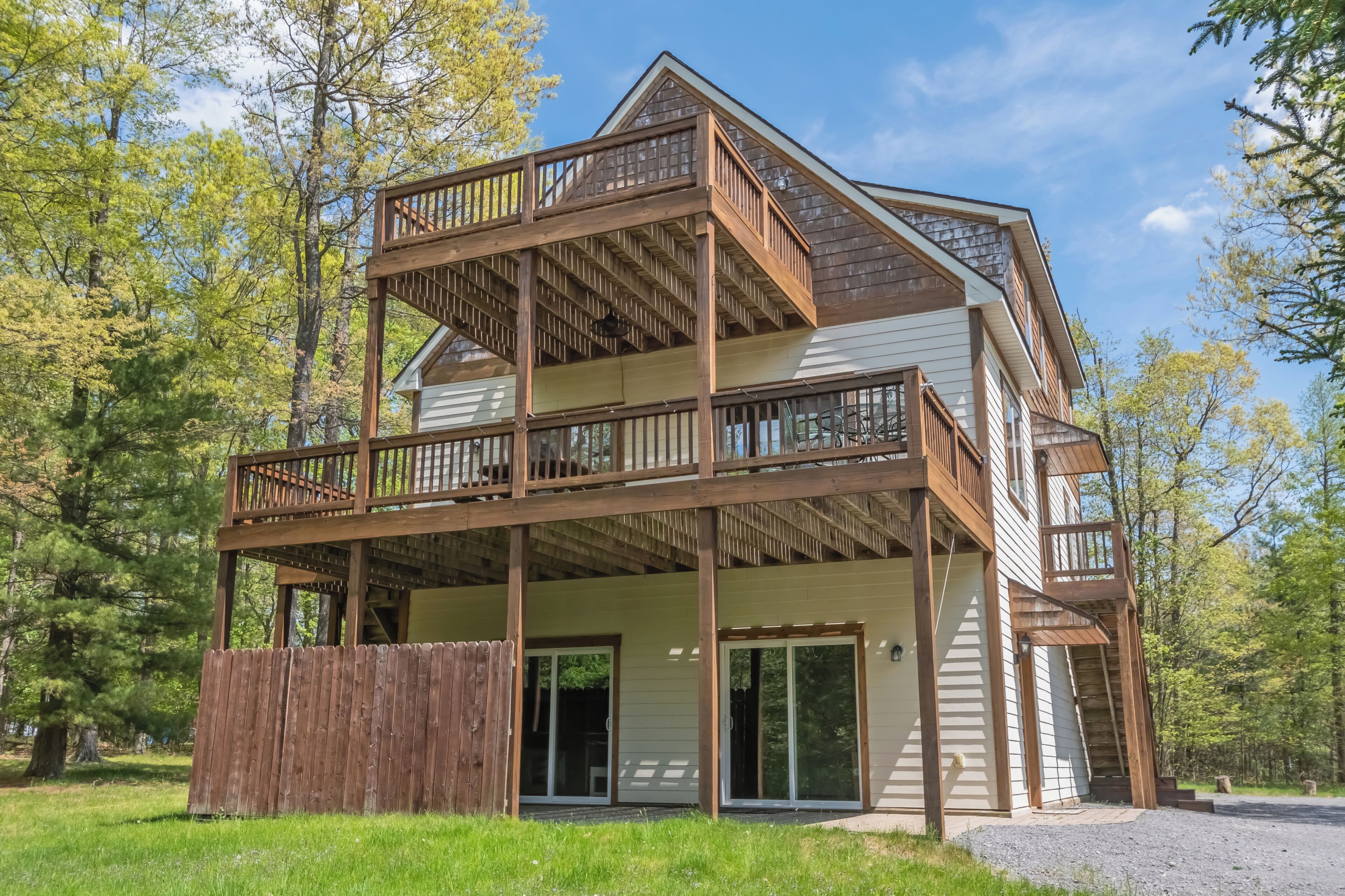 A two-story wooden cabin with a balcony, surrounded by trees.