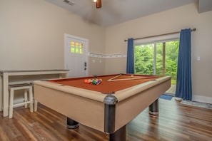 A pool table with balls, a small stool, and a door with a window.