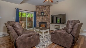 A living room with a stone fireplace, leather recliners, a TV, and a ceiling fan. - Carmel Sunday by Taylor Made Deep Creek (Swanton)