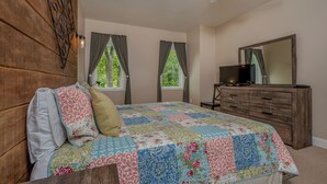 A bedroom with a wooden headboard, a quilted bedspread, a dresser, a television, and a ceiling fan. - Carmel Sunday by Taylor Made Deep Creek (Swanton)