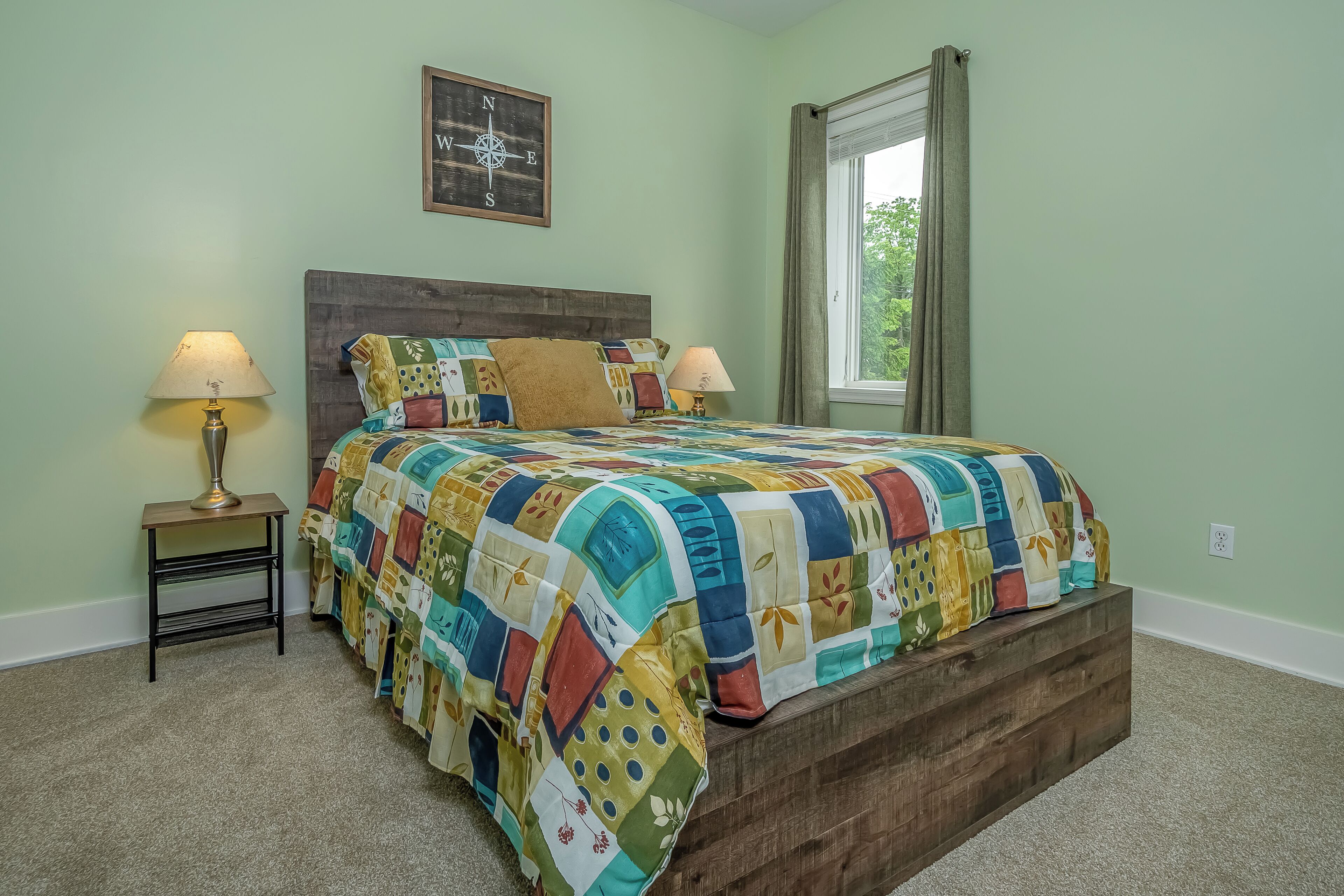 A bedroom with a wooden headboard, a colorful quilt, two bedside lamps, and a compass wall art.